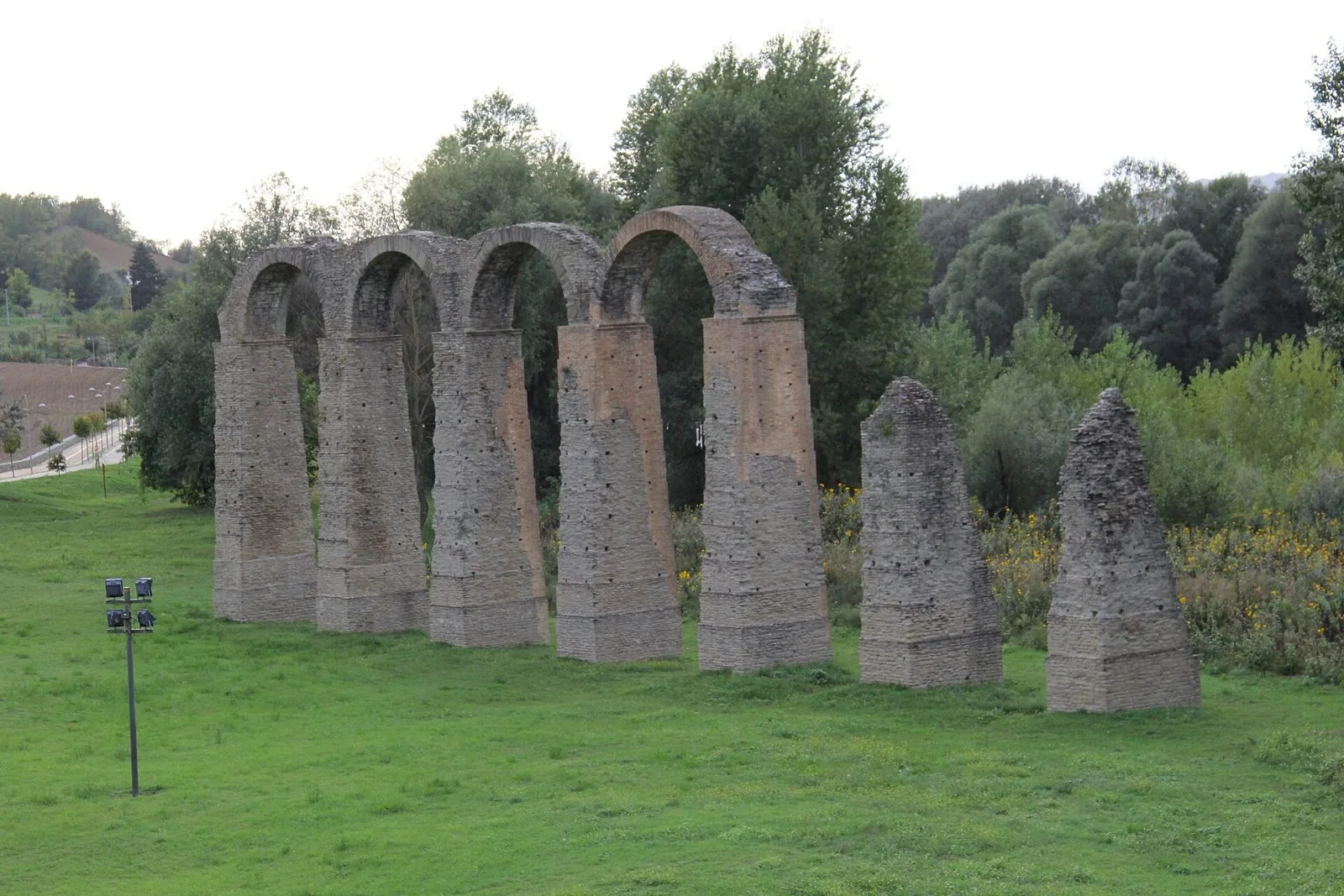 Gli archi in pietra e mattoni dell'acquedotto romano di Acqui Terme su un prato verde